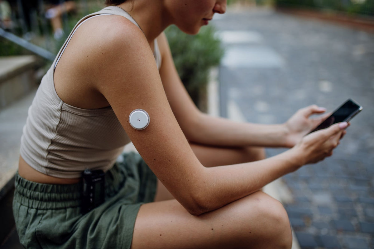 Lady sitting outdoors using a smartphone with a Glucose Monitor on their arm.