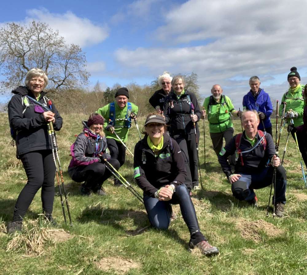 Group of Total Body Walkers posing outdoors with poles on a sunny day.