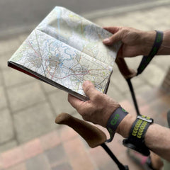 Hands holding a map with a pair of WALX Detachable wrist straps holding walking poles in place
