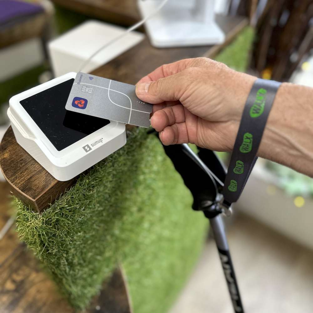 Hand holding a card above a payment terminal with a WALX Detachable wrist strap holding walking poles 