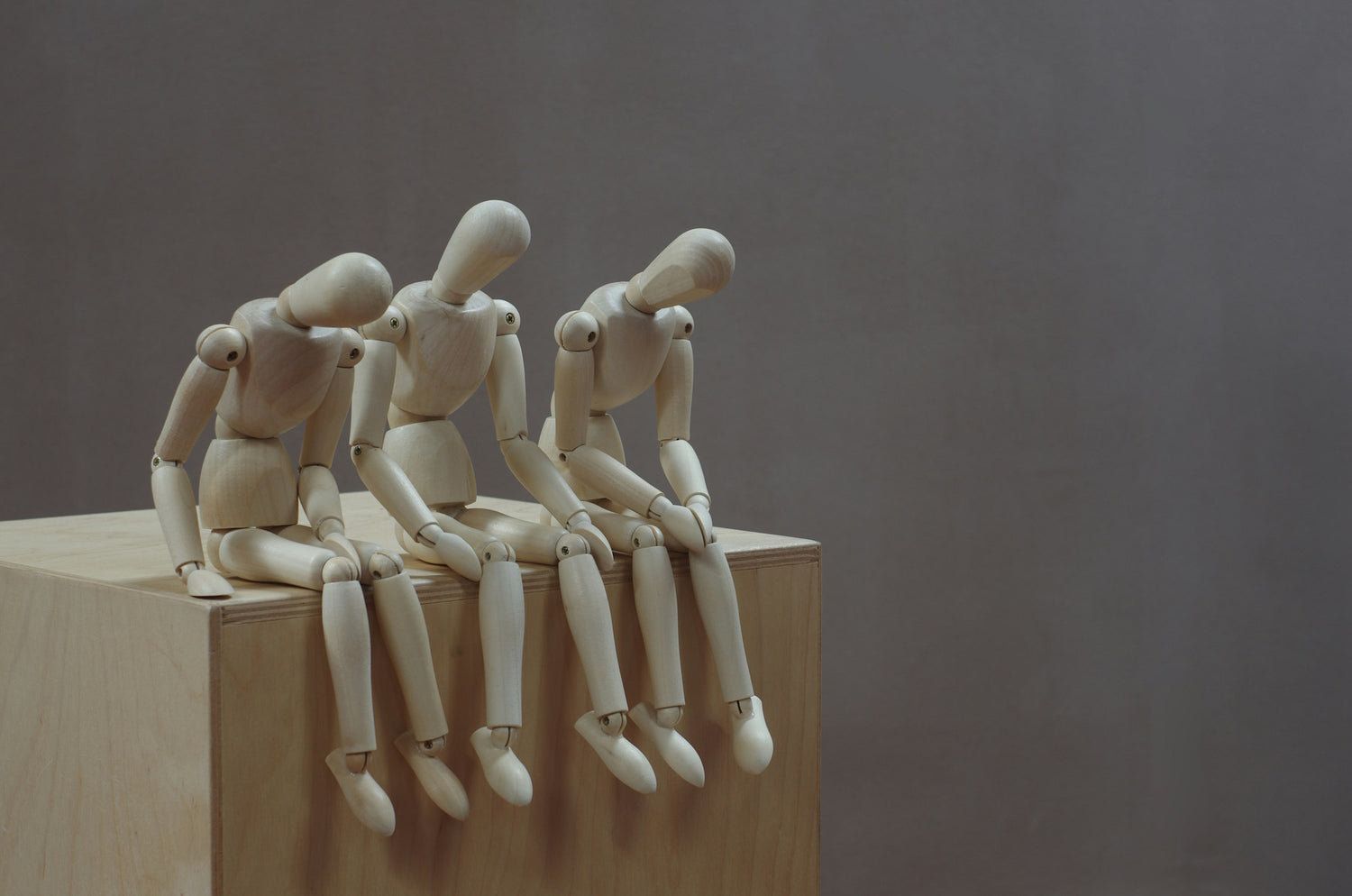 Wooden mannequin figures sitting on a wooden block against a plain background
